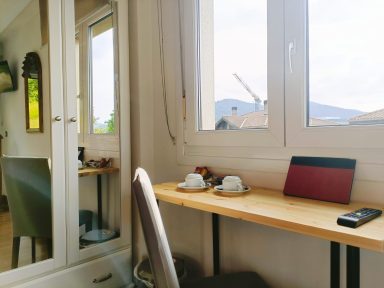 Ventana habitación 102 y detalles Escritorio con dos tazas, un teléfono y una ventana que muestra un paisaje montañoso.