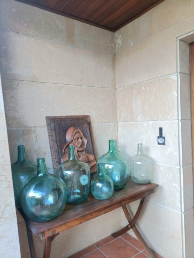 Damajuanas que nos dan la Bienvenida a casa Botellas de vidrio verde dispuestas en una mesa de madera en una esquina decorativa.