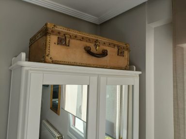 Detalle habitación 102 Maleta antigua de color claro sobre un mueble blanco con espejos.